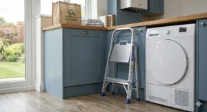 A compact 2-step domestic folding stool stored neatly next to a washing machine in a British utility room.