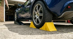 Close-up photograph illustrating safety features with car ramps, showing yellow wheel chocks securely positioned around a rear tyre on a UK driveway.
