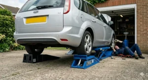 Heavy-duty blue hydraulic lifting car ramps elevating a silver Ford Focus estate for underside servicing on a residential UK driveway.
