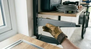 A close-up view of a hand securely fastening a bracket to the upright of a heavy-duty garage shelving system.