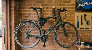 A hybrid bicycle hanging horizontally by its top tube from padded wooden wall hooks inside a tidy, compact workshop garage.