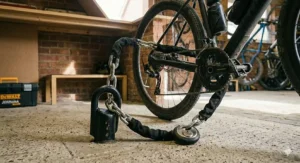 A high-security heavy-duty ground anchor and thick gold-rated chain securing a bicycle to the concrete floor of a residential garage.
