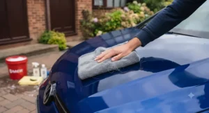 Buffing cured car wax off paintwork with a clean microfibre cloth to reveal a deep, reflective gloss finish.