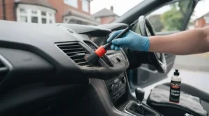 Soft detailing brushes cleaning air vents and dashboard buttons on a car interior.