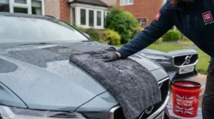 Drying a vehicle’s paintwork after a wash using a large, plush microfibre drying towel to leave a streak-free finish.