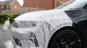 Applying snow foam to a black car as part of a safe pre-wash routine to prevent paintwork swirl marks.