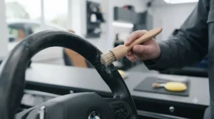 Deep cleaning a greasy leather steering wheel with a detailing kit brush to restore its natural matte finish.