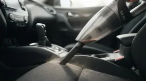 Detailed view of a portable car vacuum crevice tool cleaning deep between car seat gaps.