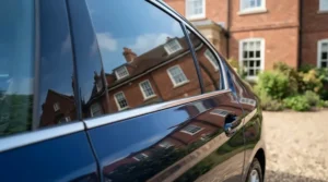 Assessing the high gloss shine in a ceramic coating vs wax comparison on a dark hatchback parked on a street.